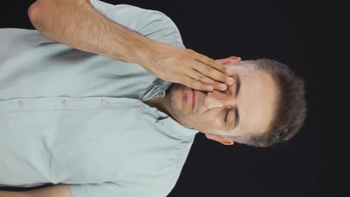 Man Rubbing Eyes on Black Background, Portrait Orientation