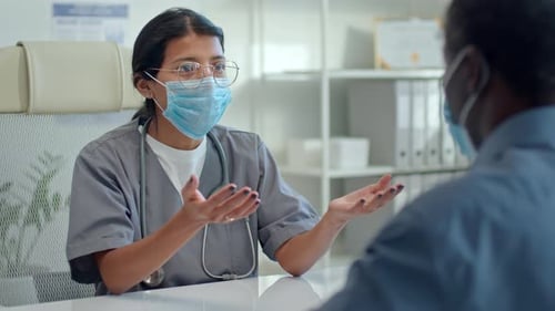 Female Doctor in Face Mask Talking to Patient in Medical Office