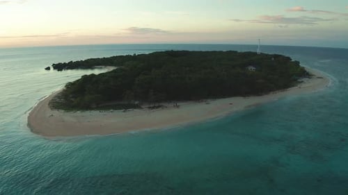 Remote island in Philippines during sunset with blue waters and a sandy beach.