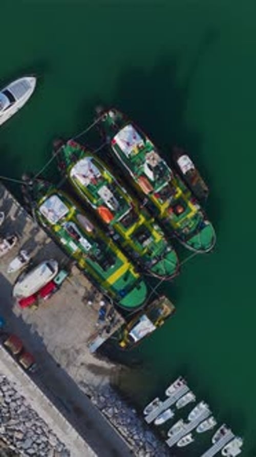 Vertikales Video von Schleppern, die in der Nähe eines Containerterminals festgemacht haben, von oben aufgenommen, bereit für ihren nächsten