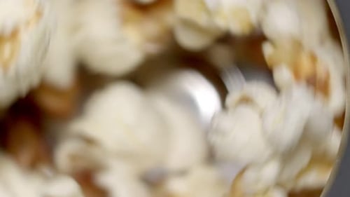 Close up top view: Puffed white popcorn spins in hot air popper, slo mo.