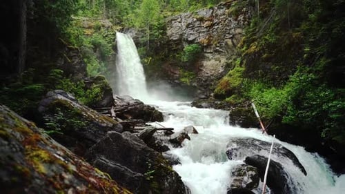 Pan up revealing slow motion water rushing over rocks with a waterfall on top