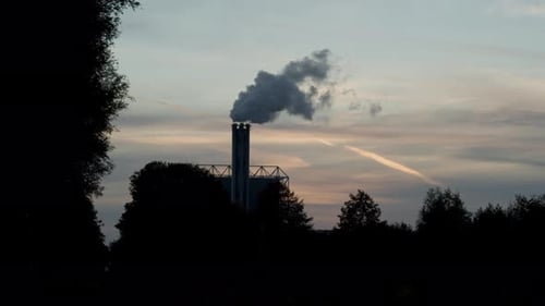 Beautiful silhouette of smoking factory chimney against a sunset in realtime