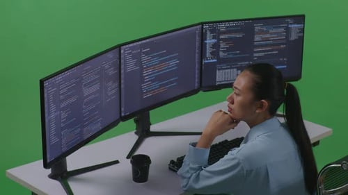 Side View Of Asian Woman Thinking While Write Code With Multiple Computer Screens In Green Screen