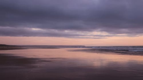 Colorful sunset on the beach timelapse. Low tide reflections as waves lap the shore