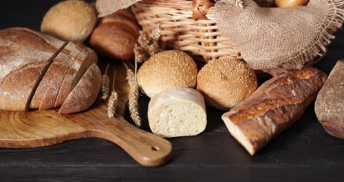 Woman taking piece of bread at black wooden table, closeup