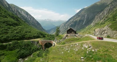 Cars Driving Through Grimsel Pass With Cabin And Rhone Valley On A Sunny Day In Switzerland. - aeria