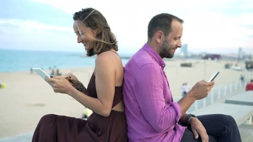 Young couple enjoying mobile technology on a summer holiday near the beach