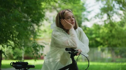 Thoughtful Woman in Raincoat Reflects By Bicycle in Green Forest