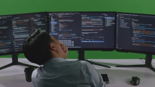 Back View Of Tired Asian Man Yawning While Write Code With Multiple Computer Screens In Green Screen