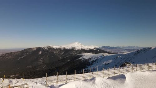 Take off aerial drone shot from a snowy road revealing an endless wild snow covered mountain range.
