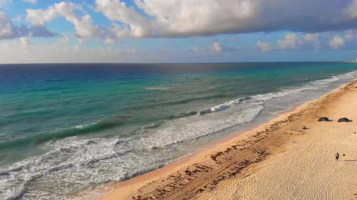 Drone panning shot of tropical sea waves crashing on white sandy shore, blue sky, sun rays shine on