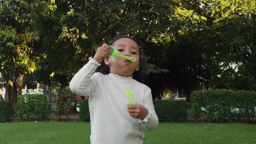 slow motion of happy toddler girl blowing soap bubbles in the park
