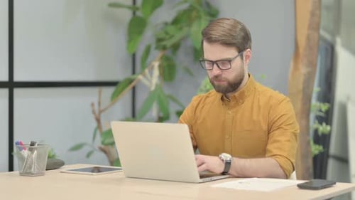 Young Man Typing on Laptop in Office