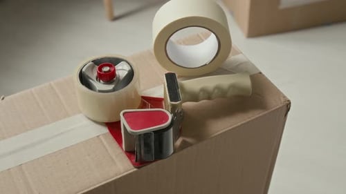 Close-up of Packing Tape Dispenser and Masking Tape on Cardboard Box