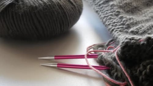 light camera movement to a dark coloured wool - knitting needle stand out of a knitted piece of text