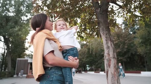 Loving mother walks with her cute daughter in the park. Mom holds her daughter in her arms, the girl