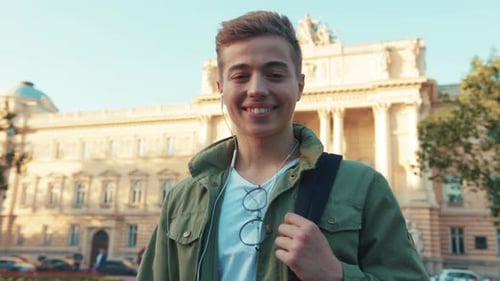 Smiling Young Man with Headphone Backpag Stand Look at Camera Feel Happy on Street Outdoors Close Up