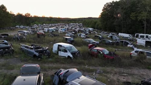 Drohnen-Tiefflug über mehrere Reihen mit zerstörten Autos und Fahrzeugen auf Schrottplatz. Sonnenuntergangszeit in