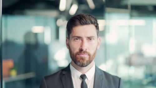 portrait of confident business man in formal suit standing in modern glass office looking at camera.