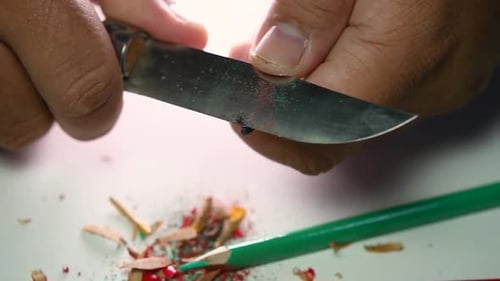 Hands Sharpening a Colored Pencil with Knife