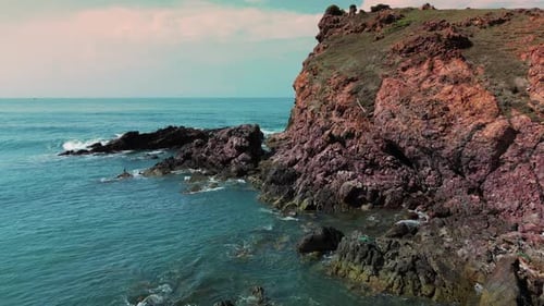 Top View Colorful Waters of the Ocean Swirl Around the Rocky and Scenic Coastline Sea Waves Breaking
