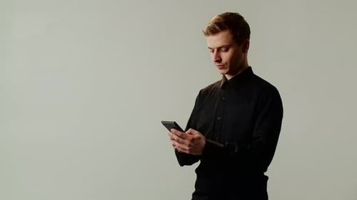 Young Serious Businessman Standing Indoors with Smartphone Male Student in Black Shirt Texting