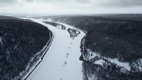 Aerial view of a bending snow covered river and forested valley. Frozen curving river flowing