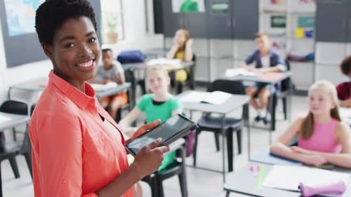 Portrait of diverse female teacher and happy schoolchildren at desks in school classroom