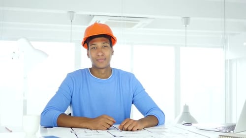 Architect Smiling at Desk with Blueprints in Office