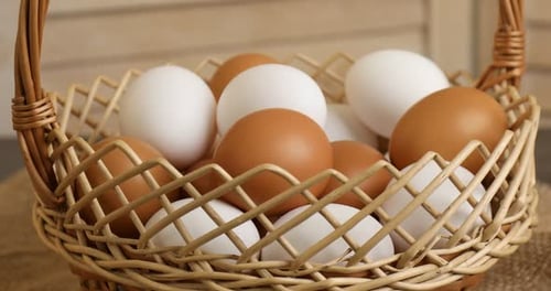 Woman putting raw chicken eggs into wicker basket at table, closeup