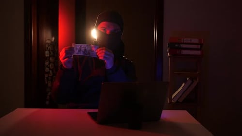 Masked Figure with Money and Laptop in Dark Room