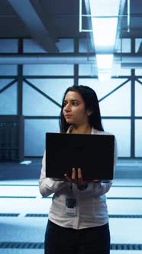 Vertical Video Programmer Walking in Data Center Coding on Laptop