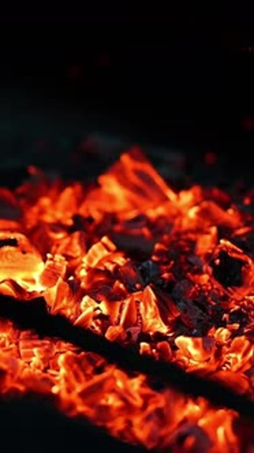 Burning up logs on campfire. Detailed motion of fire on black wood smoldering.