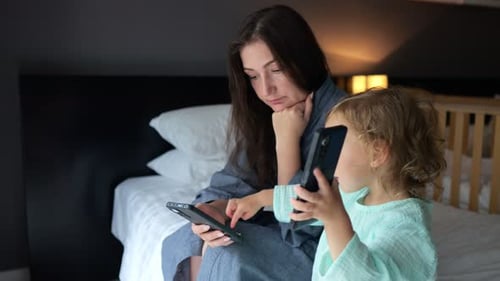 Mother and Child Looking at Smartphones on Bed