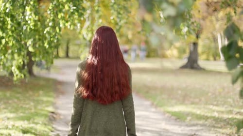 4K Slow Motion: Beautiful young redhead woman walking away. In a park on a sunny autumn evening with