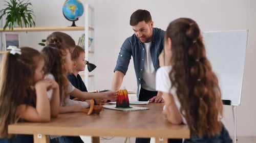 Model of the volcano is on the table. Group of children students in class at school with teacher