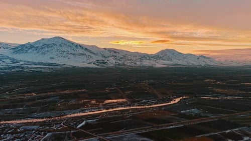 Aerial View of Snowy Mountains, River and Winter Farmland at Sunset