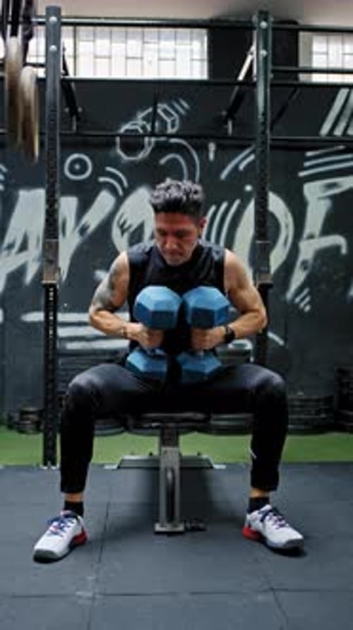 Young Man Lifting Dumbbells in Gym on Bench