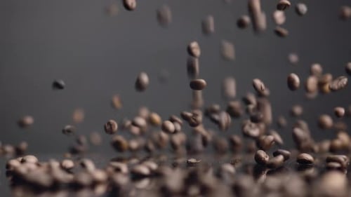 Braune Kaffeekörner, die auf die Oberfläche fallen und prallen, Nahaufnahme. Geröstete aromatische Samen im Morgengrauen in Super
Sl...
