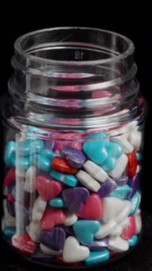 Multicolored sugar hearts in a jar for decorating pastries are spinning in a loop on a black.