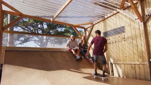 Video of happy diverse female and male skateboarders training in skate park