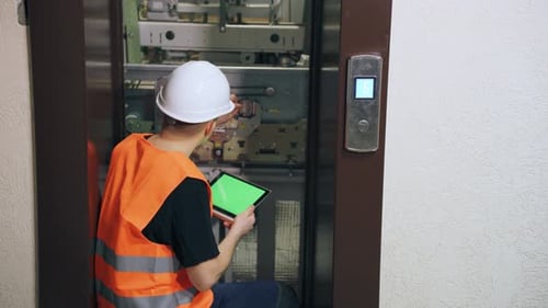 Engineer Repairs Elevator Using Tablet with Green Screen
