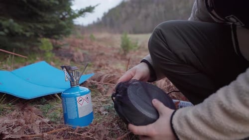 Man With Portable Camping Burner Is Setting To Boil Water Near Forest Mountains. Close Up