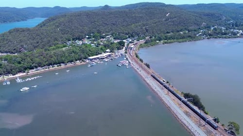 Drone aerial landscape of commuter train approaching Hawkesbury River railway station near rural