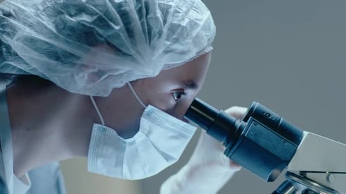 Female Scientist in Mask and Gloves Looking in Laboratory Microscope
