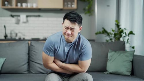 Man Clutching Stomach in Pain on Couch Indoors