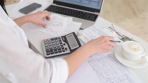 Frau arbeitet mit Finanzpapieren auf weißem Schreibtisch und Laptop zählt auf dem Taschenrechner