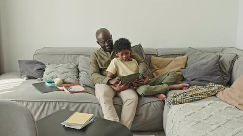 Father and Son Looking at Tablet on Sofa