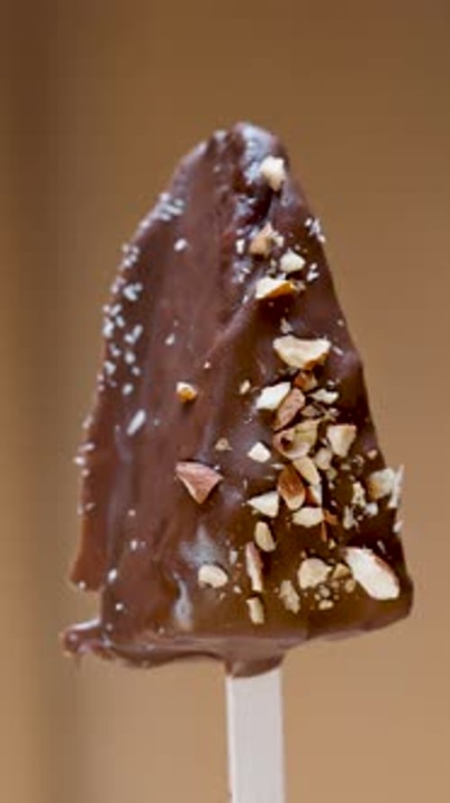 Chocolate cake in the form of Ice cream on a stick, sprinkled with almonds, rotates close-up.